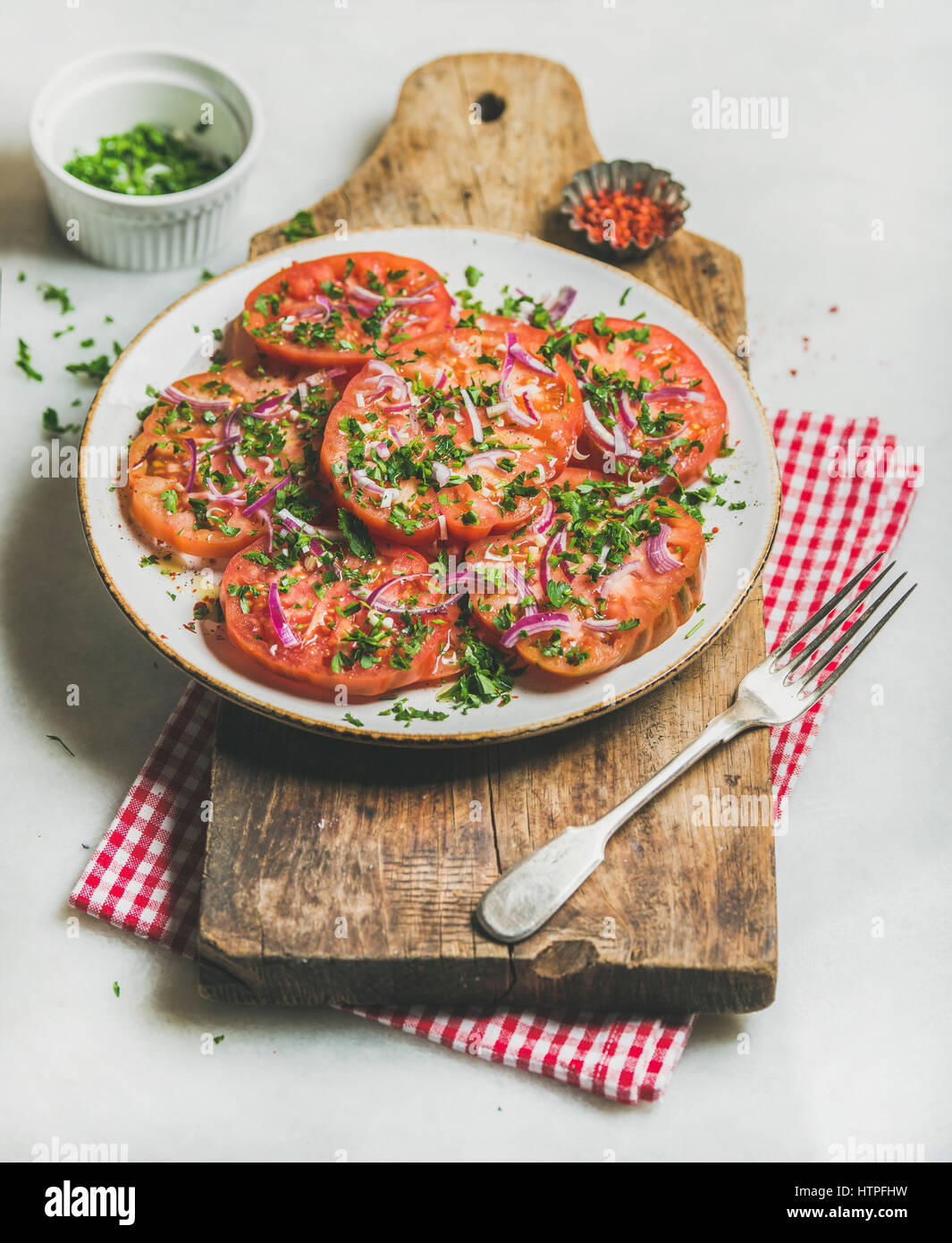 Fresh heirloom tomato, parsley and onion salad in white round plate on wooden board over light grey marble background, selective focus. Clean eating, Stock Photo