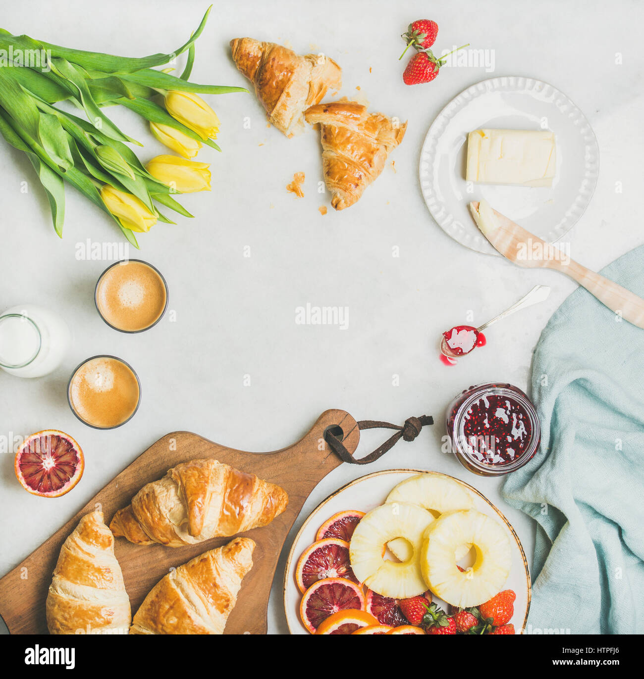 Breakfast table with croissants, butter, raspberry jam, fresh fruit, milk in bottle, coffee espresso and spring yellow tulip flowers. Top view, copy s Stock Photo
