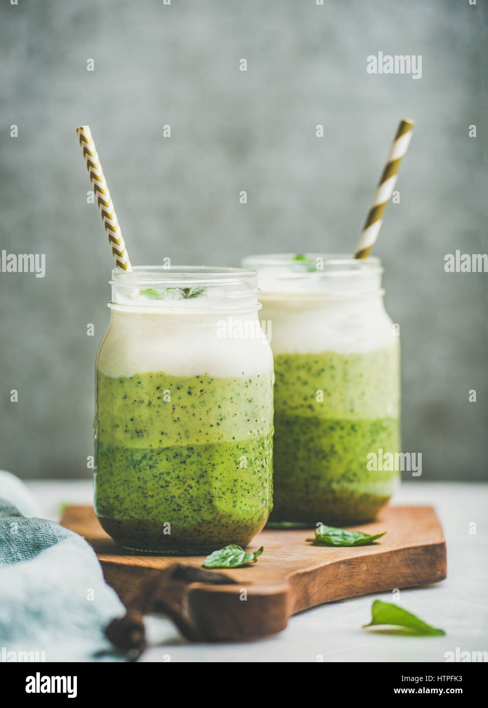 Ombre layered green smoothies with fresh mint and straws in glass jars, grey concrete wall background, copy space, selective focus. Clean eating, vega Stock Photo