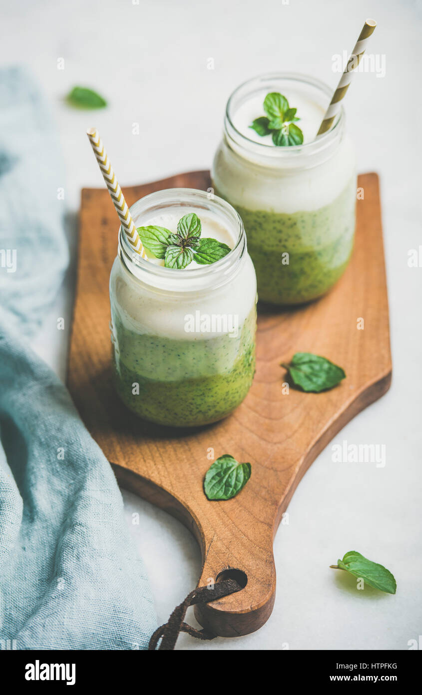 Ombre layered green smoothies with mint leaves in glass jars with straws on wooden board over light grey background, selective focus. Clean eating, ve Stock Photo