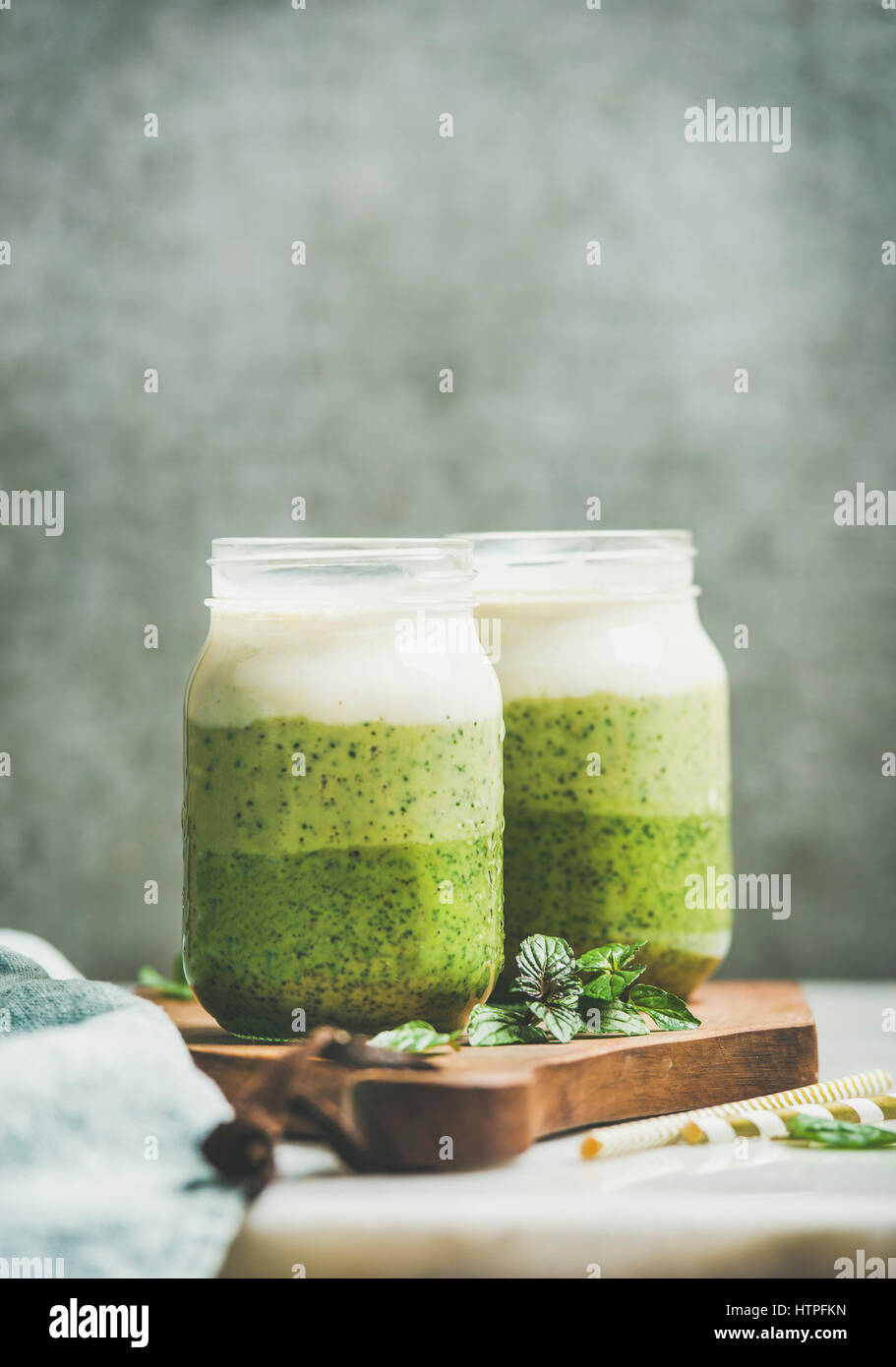 Ombre layered green smoothies with mint in glass jars on wooden board, grey concrete wall background, copy space, selective focus. Clean eating, vegan Stock Photo