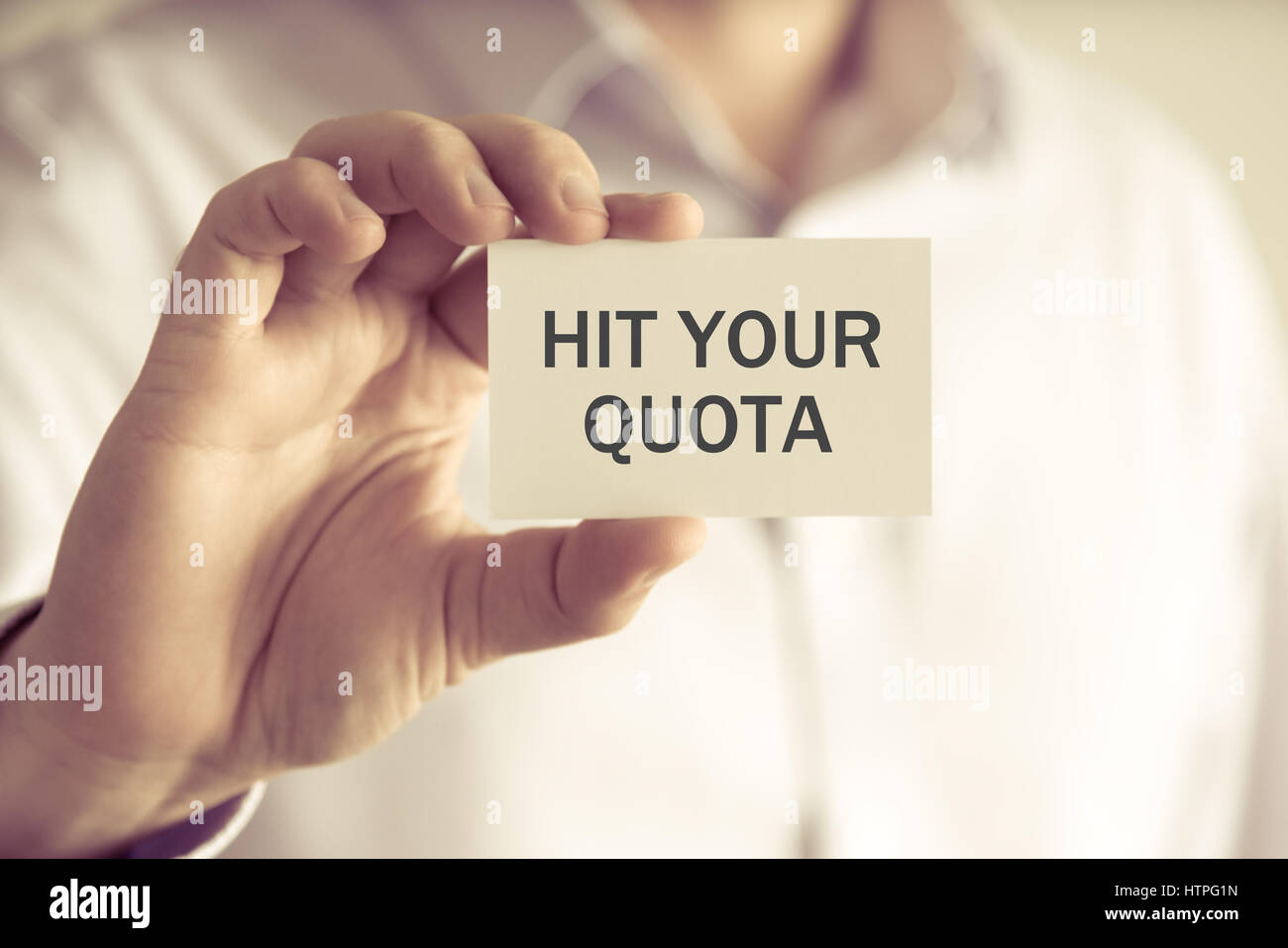 Closeup on businessman holding a card with text HIT YOUR QUOTA, business concept image with soft focus background and vintage tone Stock Photo