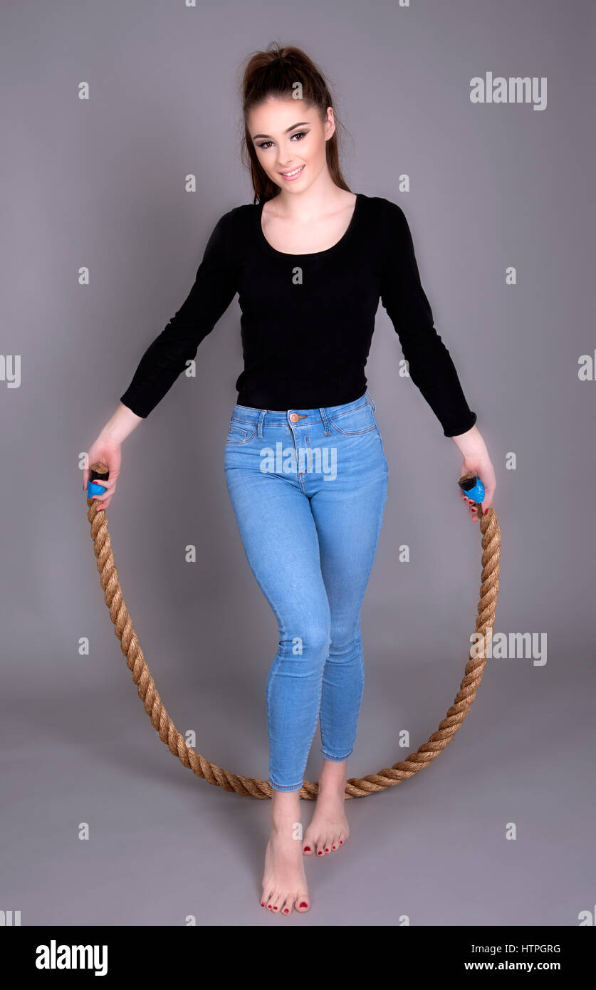 Young woman wearing jeans and a black top skipping with a thick rope