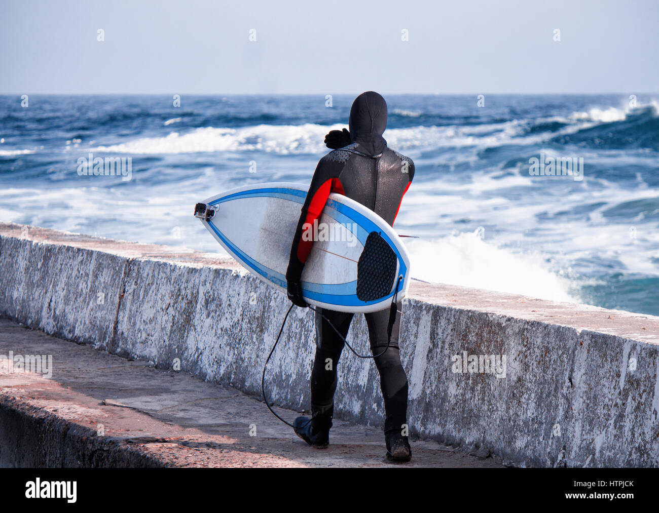 Surfer walking into water wearing a wetsuit in winter on pier. Cold
