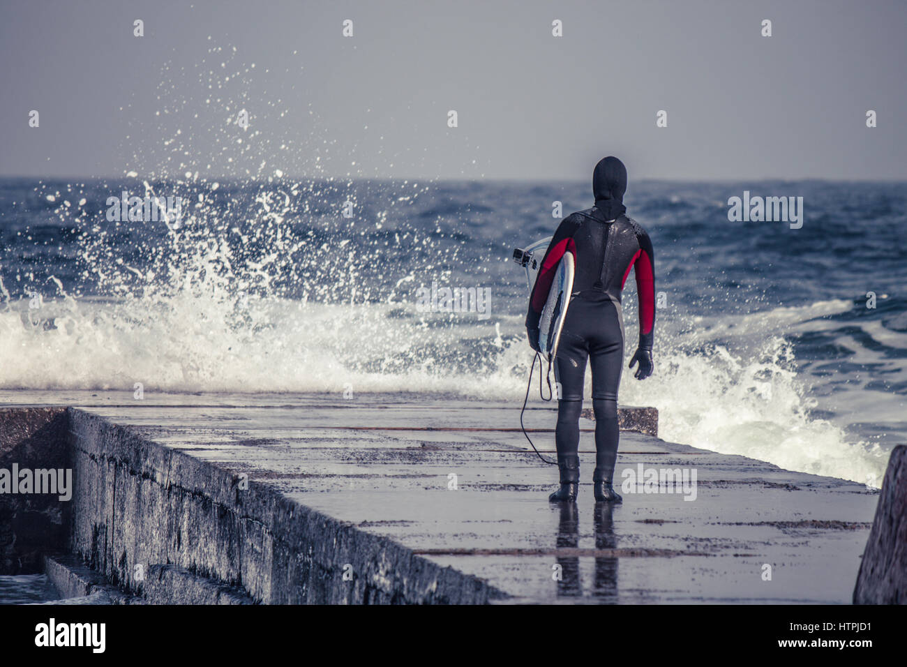 Surfer goes into water wearing a wetsuit in winter. Cold surfing. Wave
