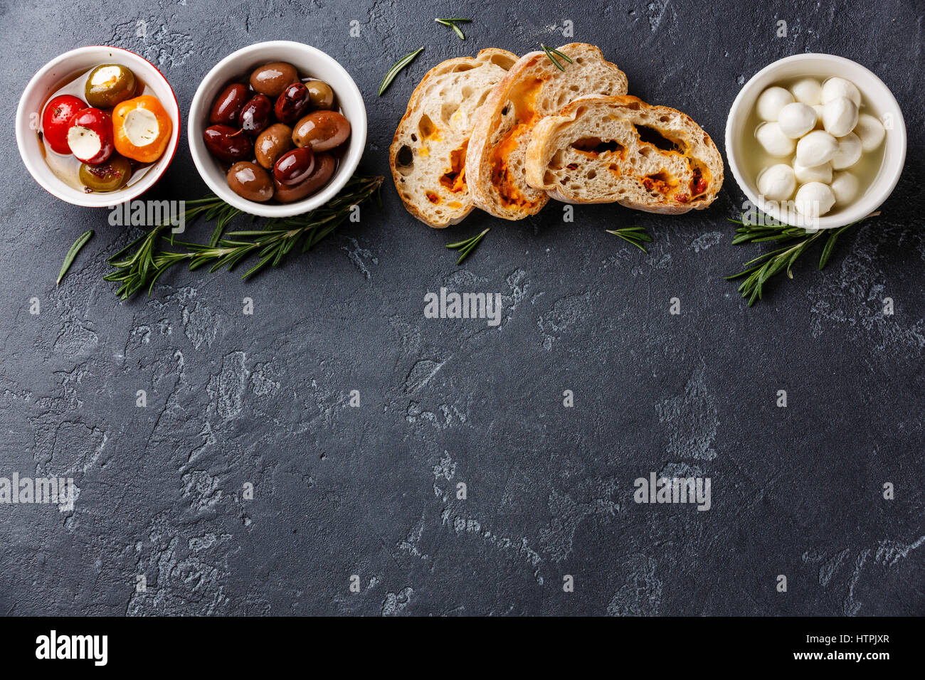 Olives, stuffed Peppers, mini Mozzarella cheese and sliced Ciabatta bread on dark background copy space Stock Photo