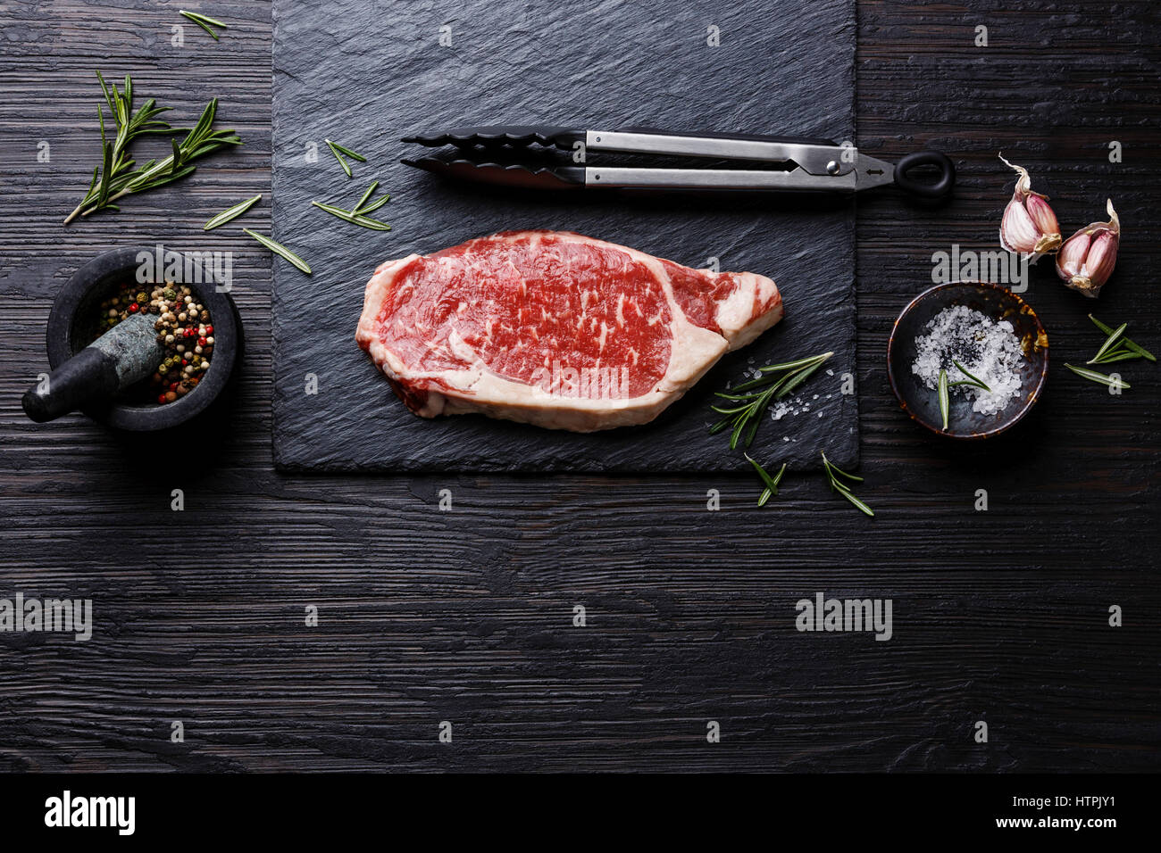 Raw fresh meat Steak Striploin and seasonings on black burned wooden background copy space Stock Photo
