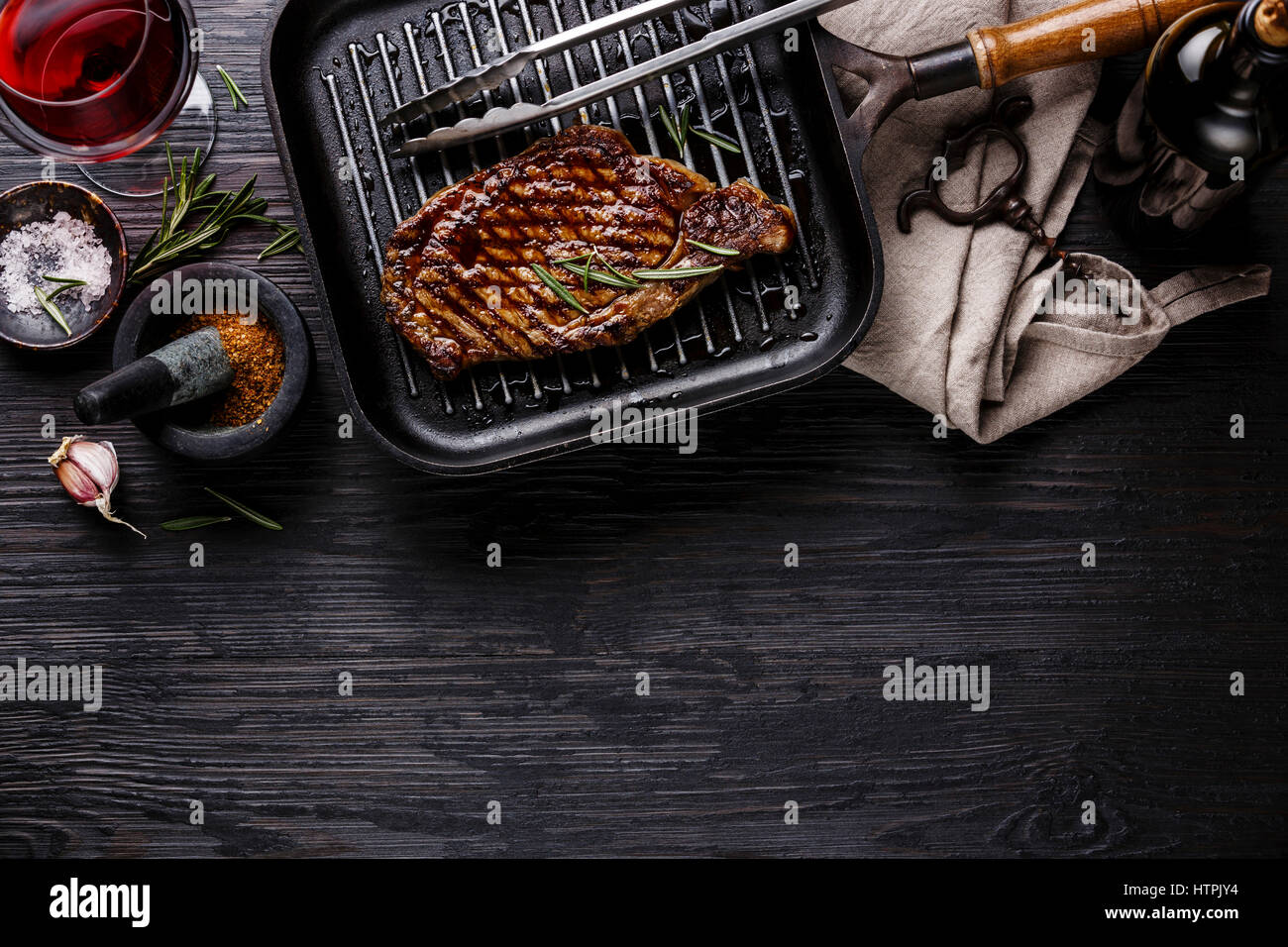 Grilled Steak Striploin on pan and red wine on black burned wooden background copy space Stock Photo