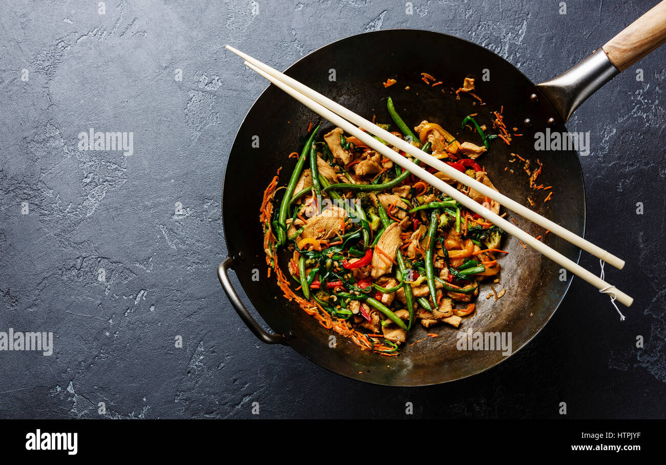 Stir fry chicken with sweet peppers and green beans in wok pan on dark stone background copy space Stock Photo