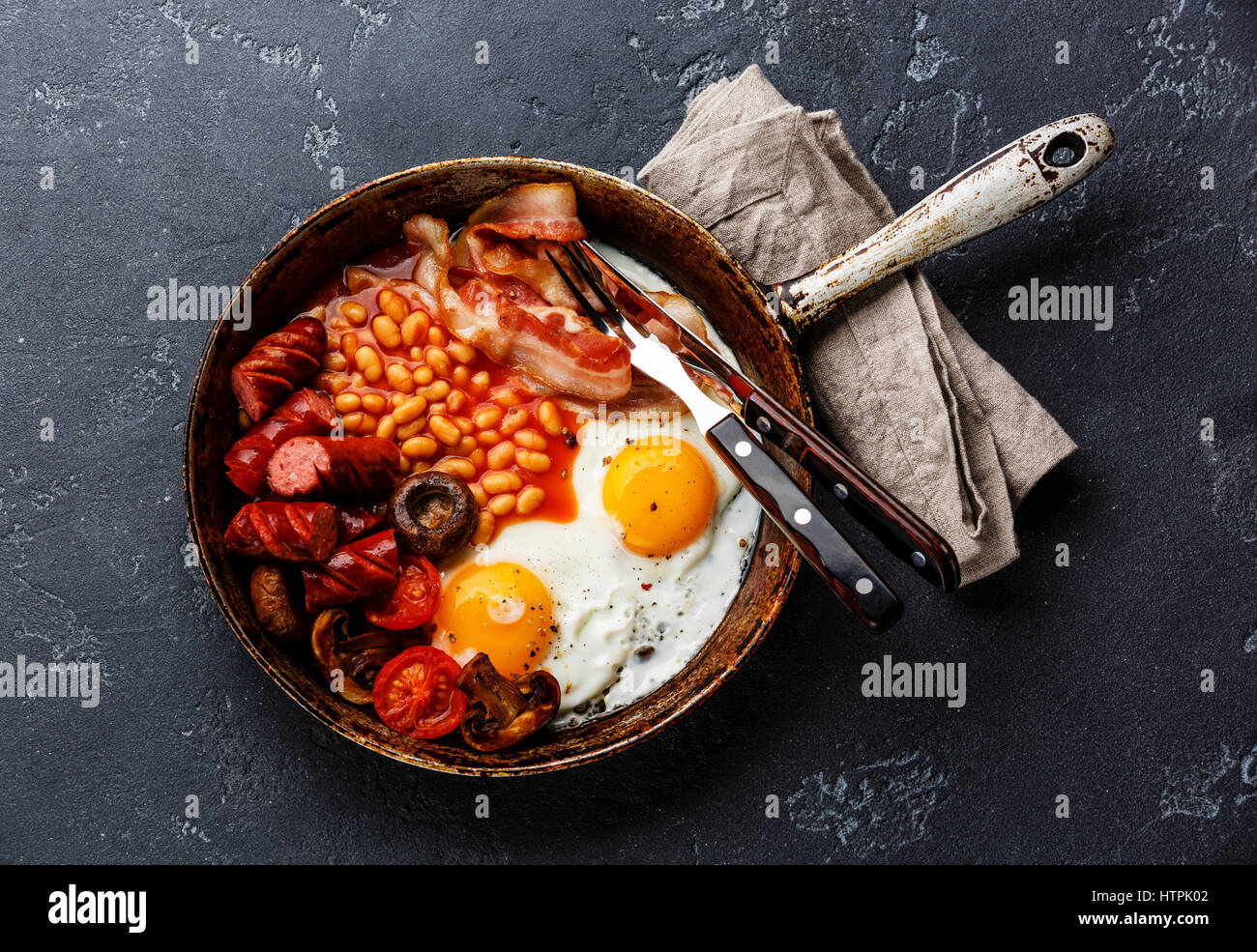 English Breakfast in cooking pan with fried eggs, sausages, bacon and beans on dark stone background copy space Stock Photo