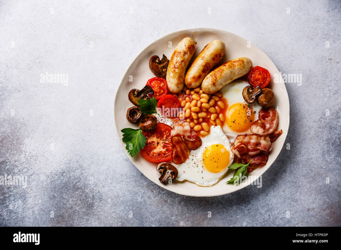 English breakfast with fried eggs, sausages, bacon, beans and bread toasts on plate on copy space background Stock Photo