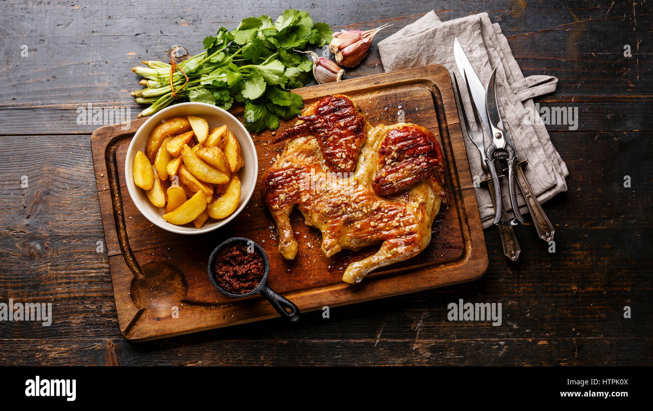 Grilled fried roast Chicken Tabaka and Potato wedges on cutting board on wooden background Stock Photo