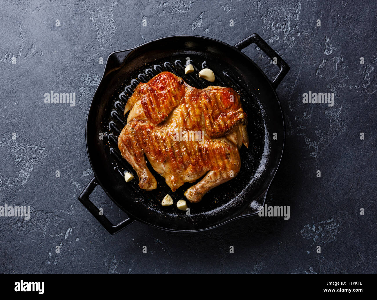 Grilled fried roast Chicken Tabaka in frying pan on dark stone background Stock Photo