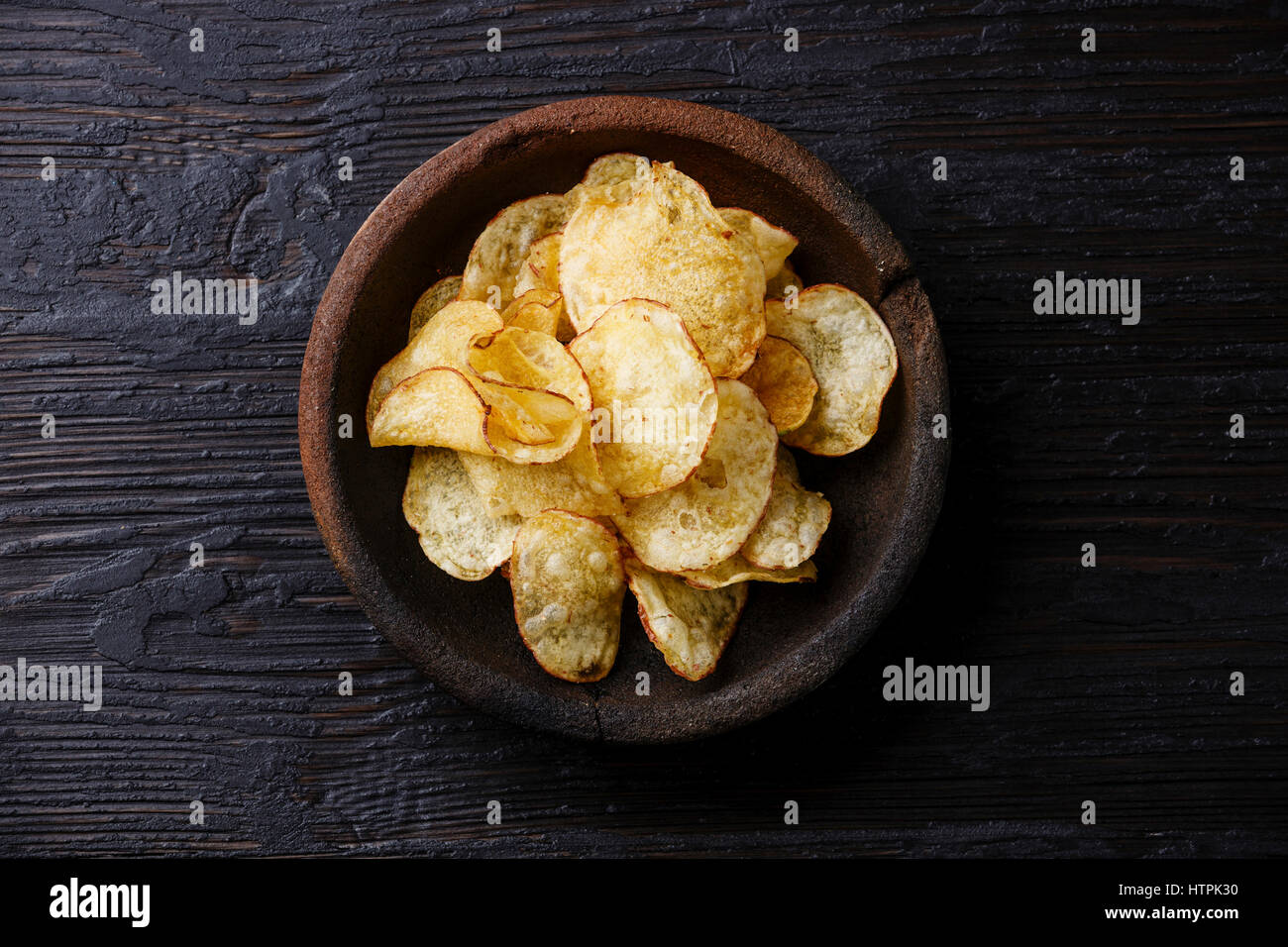 Homemade crunchy Potato chips on burned black wooden background Stock Photo