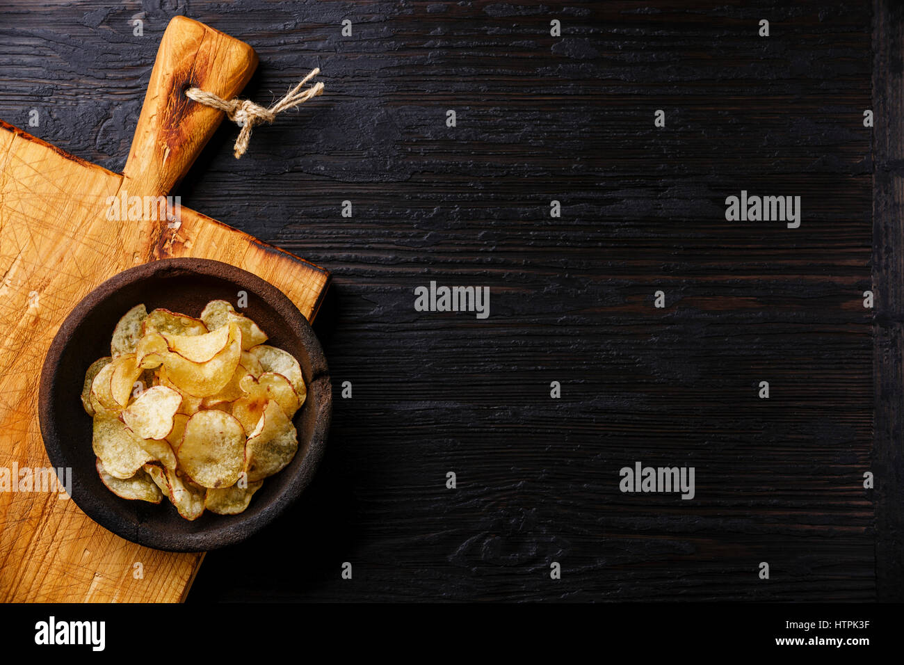 Homemade crispy Potato chips on burned black wooden background copy space Stock Photo