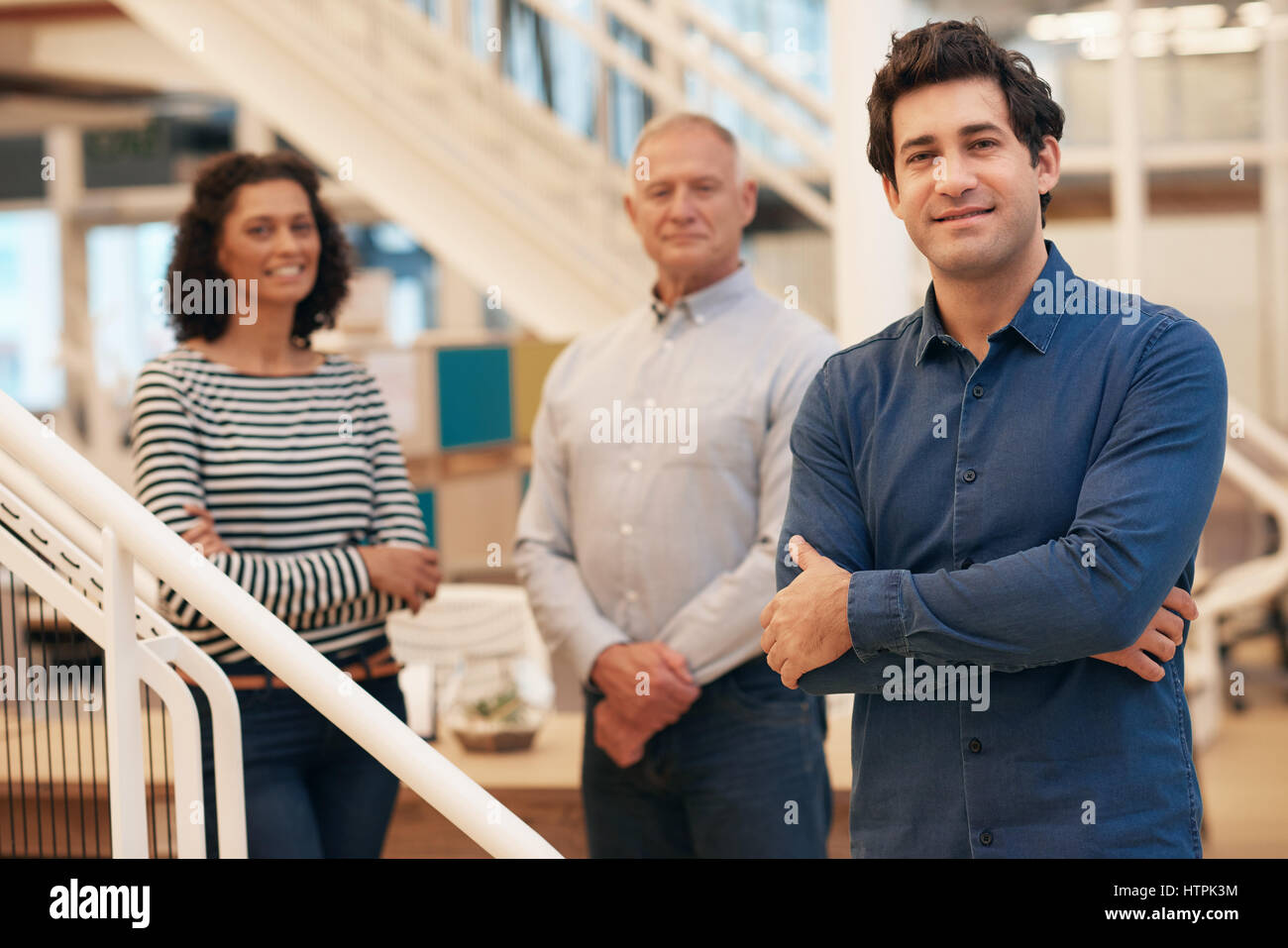Portrait of a smiling young businessman standing with his arms crossed ...