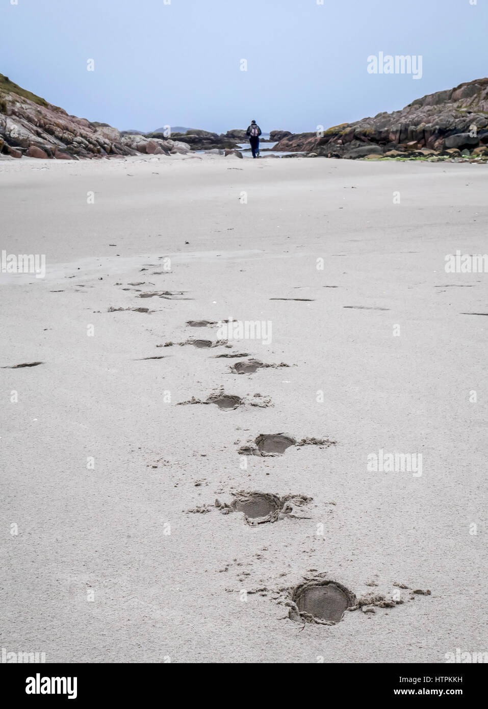 Footprints in white sand leading into distance with solitary man walking away, Isle of Mull, Scotland, UK Stock Photo