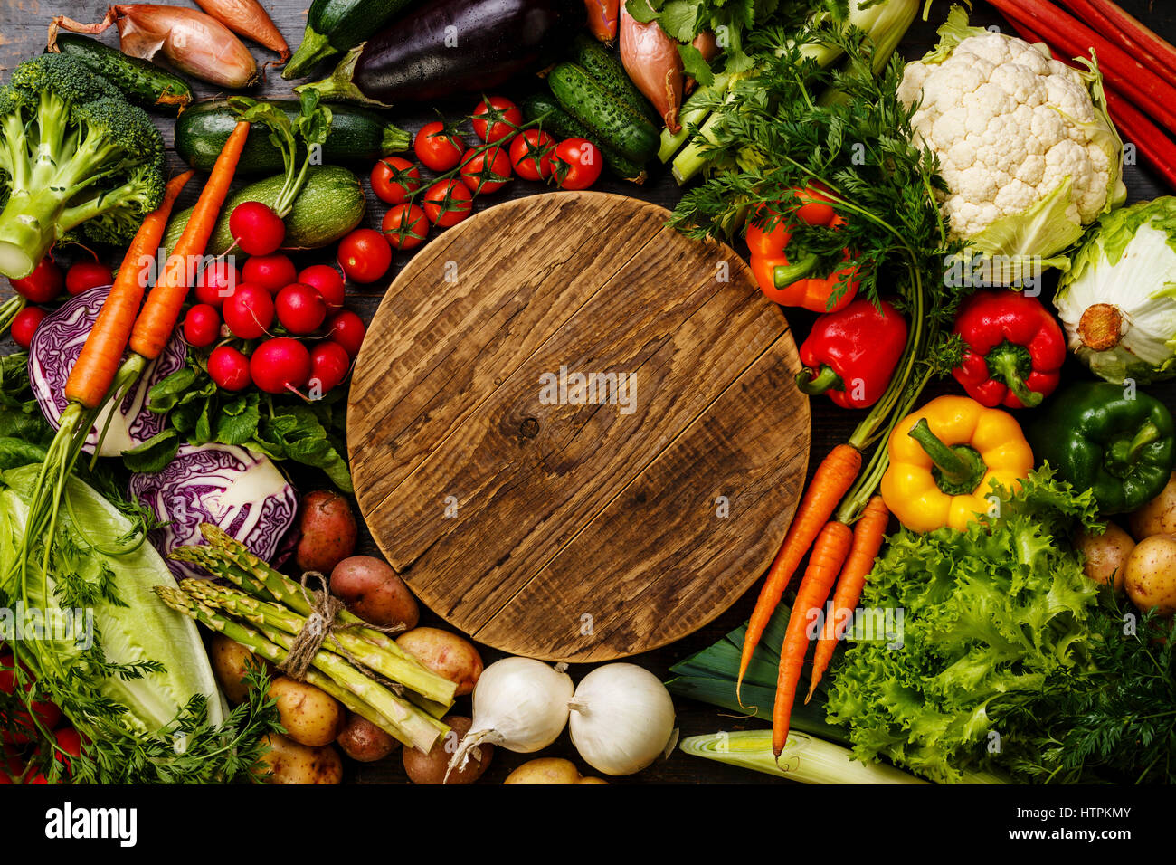 Fresh vegetables around round wooden cutting board copy space Stock Photo