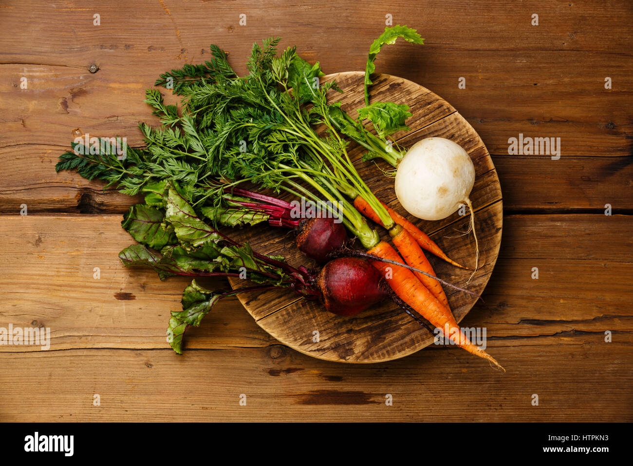 Fresh vegetables carrots, turnip and beets on round cutting board on wooden background Stock Photo