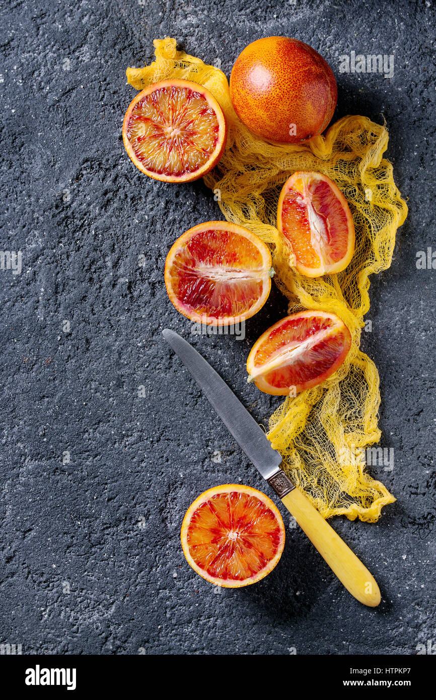 Sliced and whole ripe juicy Sicilian Blood oranges fruits with knife and yellow textile on black concrete texture background. Top view with space Stock Photo