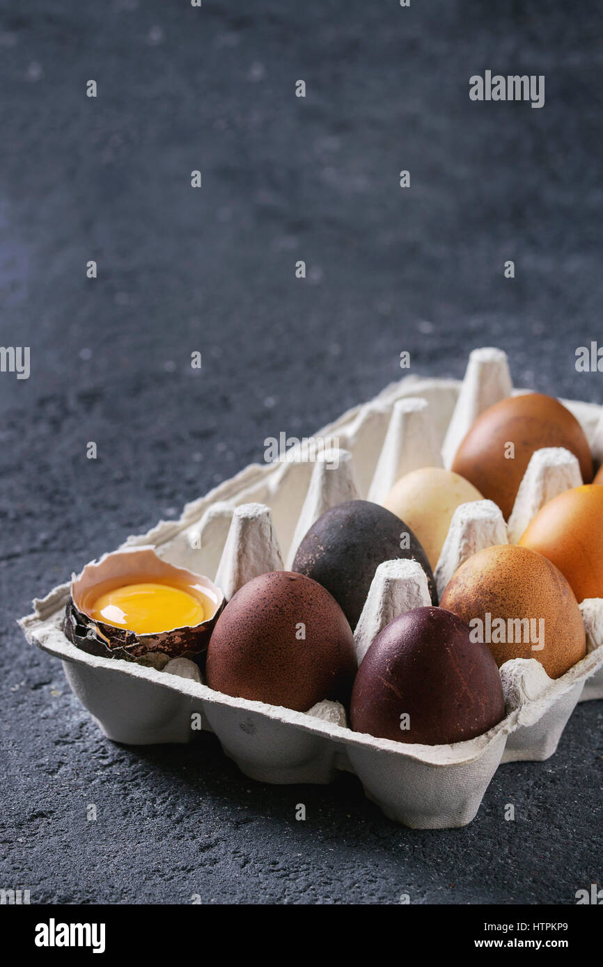Brown and gray colored chicken Easter eggs in paper box with yolk over black concrete texture background. Copy space Stock Photo