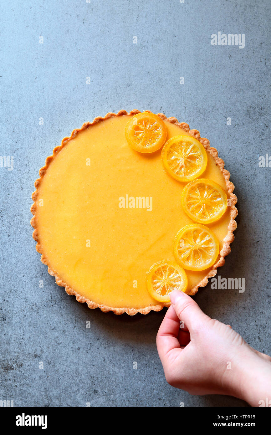 Female hand decorating a lemon tart with lemon slices.Top view Stock