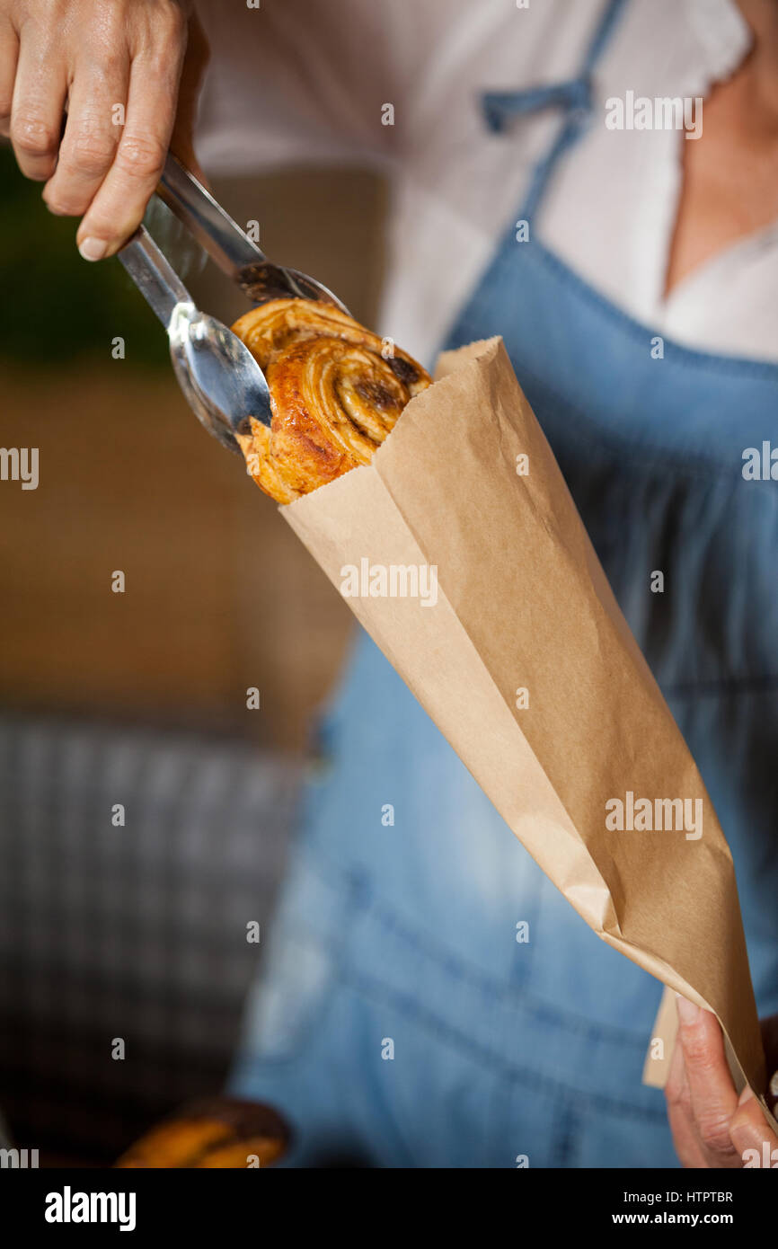 Staff Packing Mid-section of female staff packing sweet food in paper bag at ...