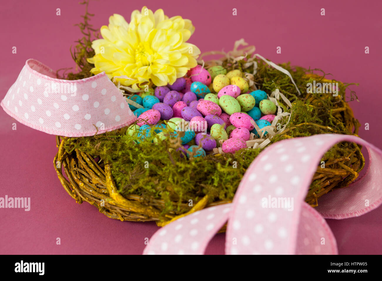 Colorful easter eggs in wicker basket with flower on pink background ...