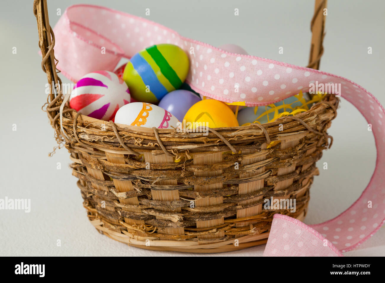 Various Easter eggs with ribbon in wicker basket on white background ...