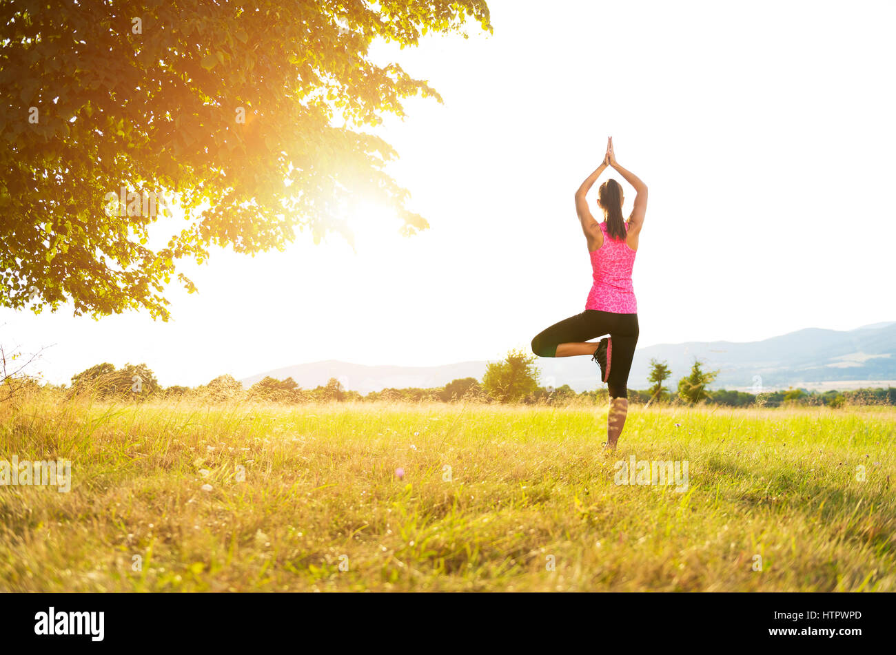 Young athletic woman practicing yoga on a meadow at sunset, image with lens flare Stock Photo