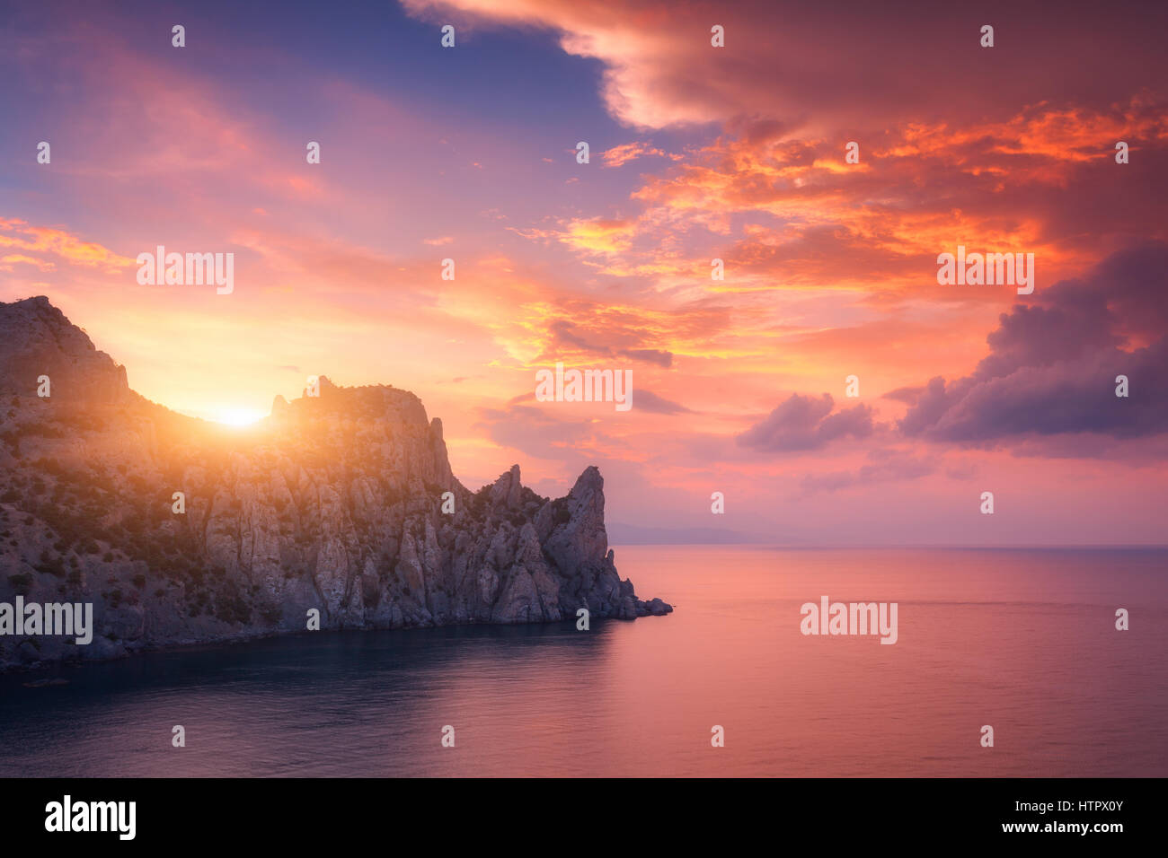 Colorful red sky. Mountain landscape at sunset. Beautiful view on the high rocks, sea, and  sky with red and orange clouds in the evening. Travel in E Stock Photo