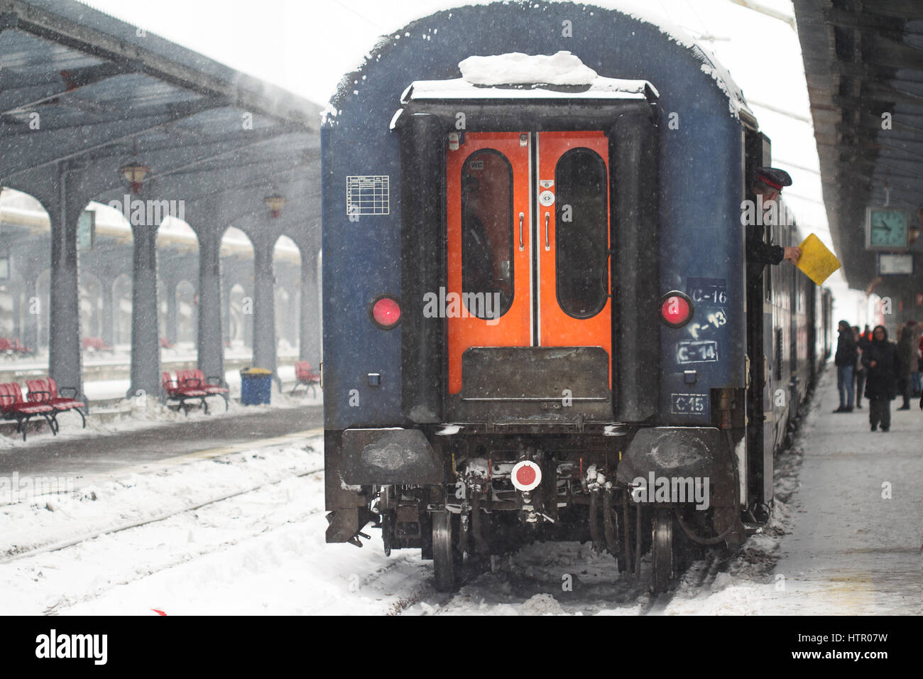Bucharest, Romania - January 7, 2017: Rear view of train conductor using a yellow flag to give the departure signal during a heavy snow storm in Bucha Stock Photo