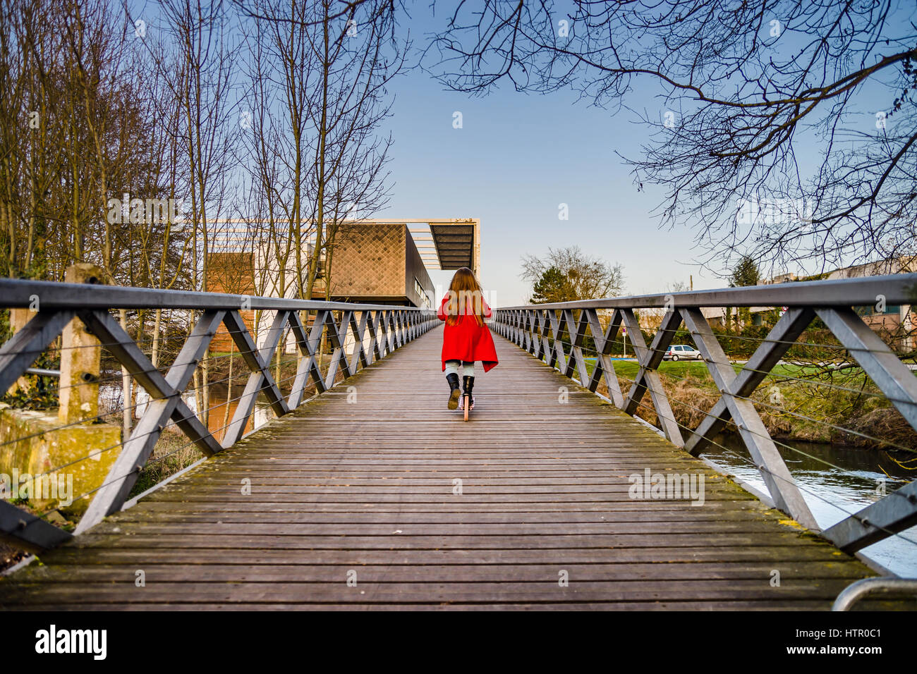 Little girl skating on the long wooden bridge over the river ...