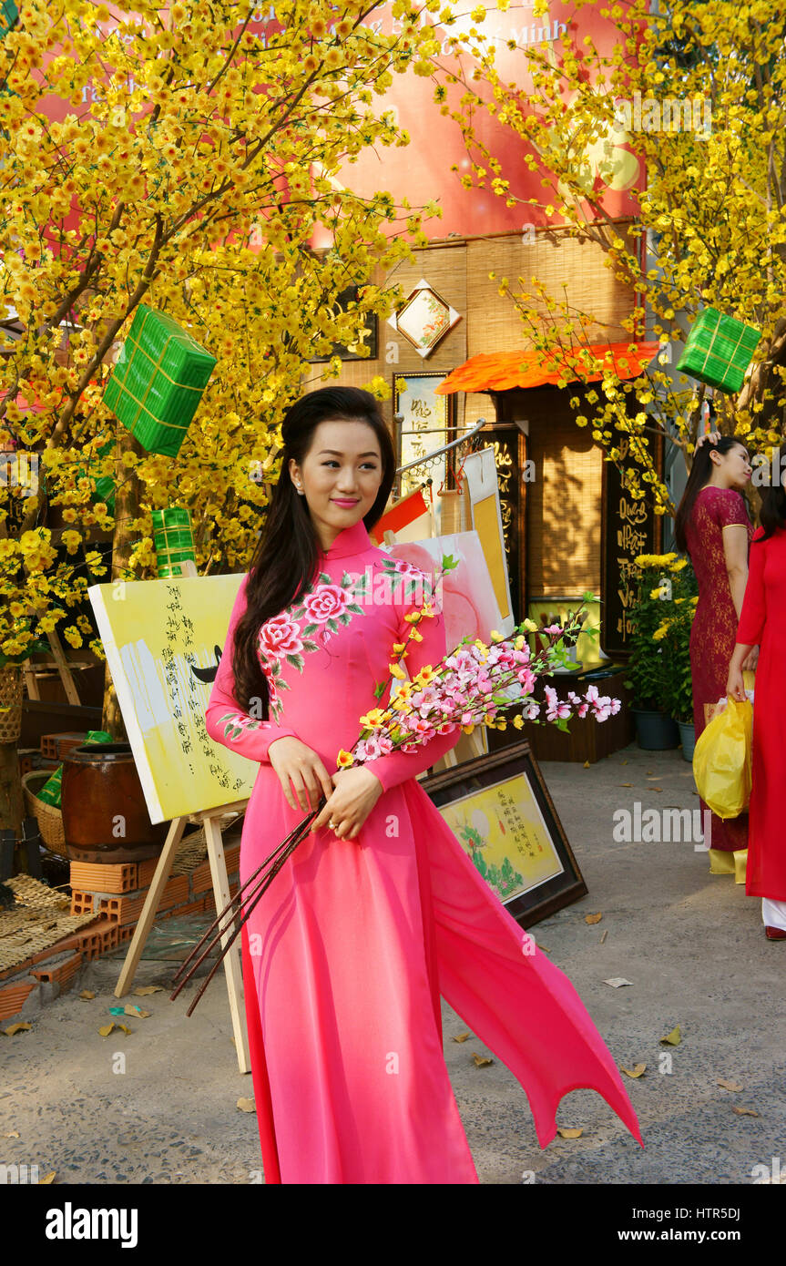 Ho Chi Minh city, Vietnam in springtime with colorful scene on Saigon street, Vietnamese woman in ao dai, posing beside flower to take photo on Tet Stock Photo