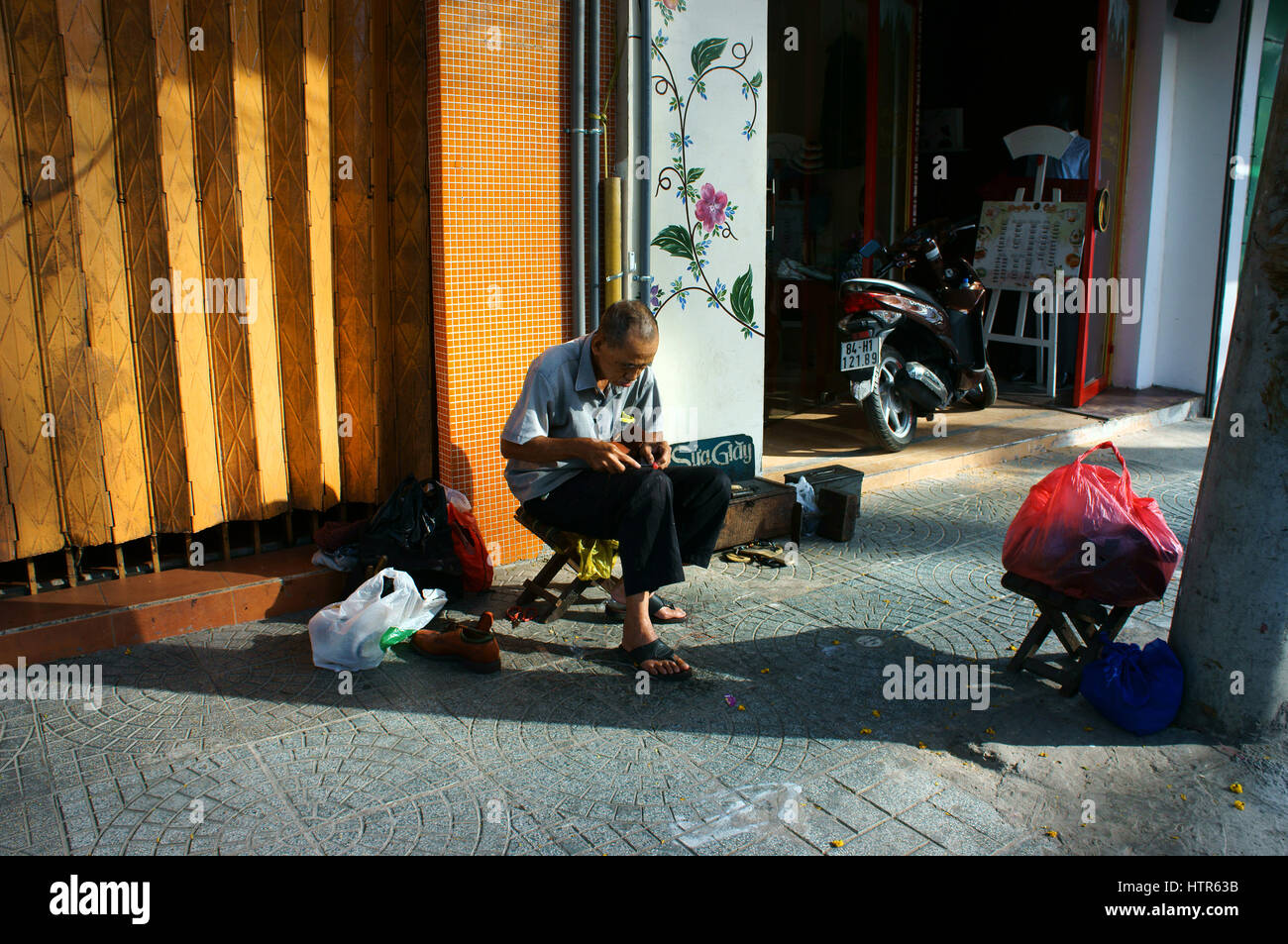 HO CHI MINH CITY, VIET NAM, senior Vietnamese man working on sidewalk, he repair shoes for customer, many poor people earning money by this, Vietnam Stock Photo