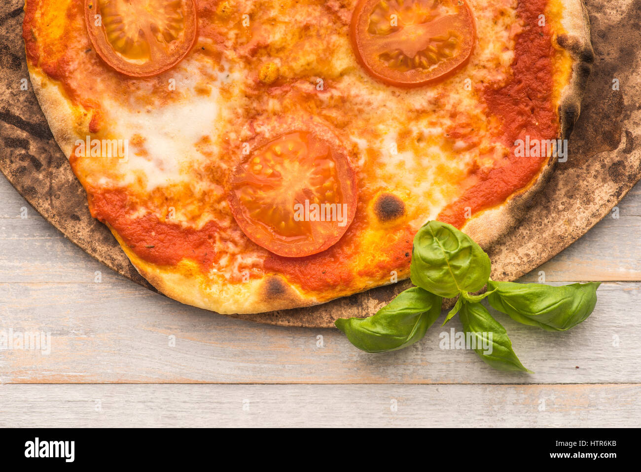 Feshly made wood fired pizza on pizza stone viewed from above on rustic grey boards Stock Photo