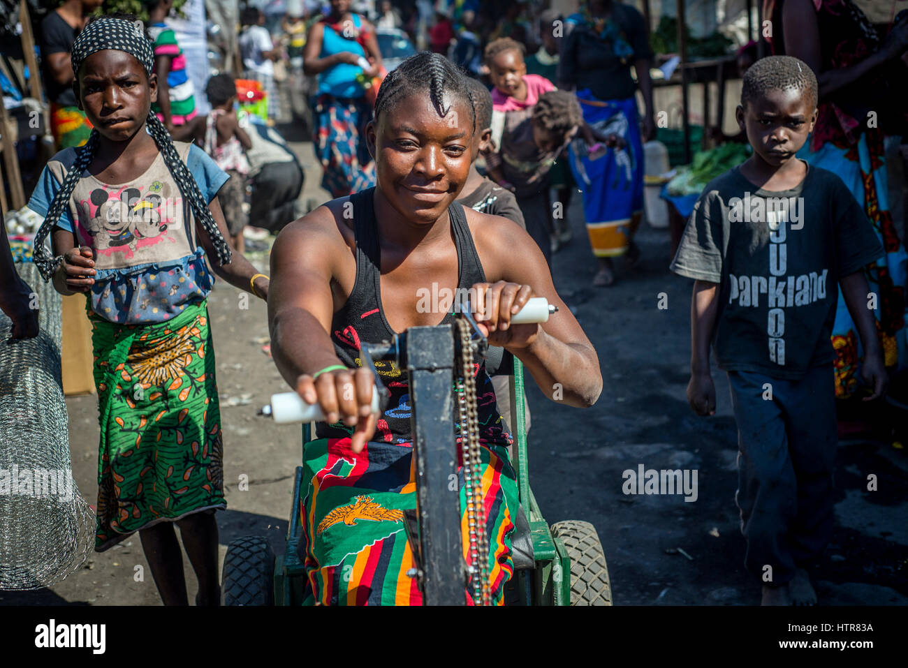 A girl rides a handbike at the local market accompanied by her friends from Home of Happiness for children with disabilities in Lusaka, Zambia. Stock Photo