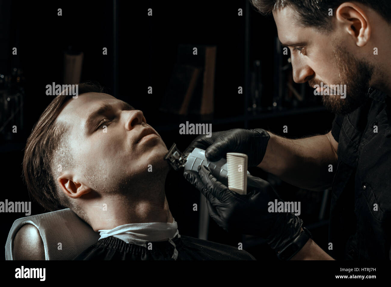 THEME. BEARDED BARBER IN BLACK RUBBER GLOVES IS TRIMMING THE