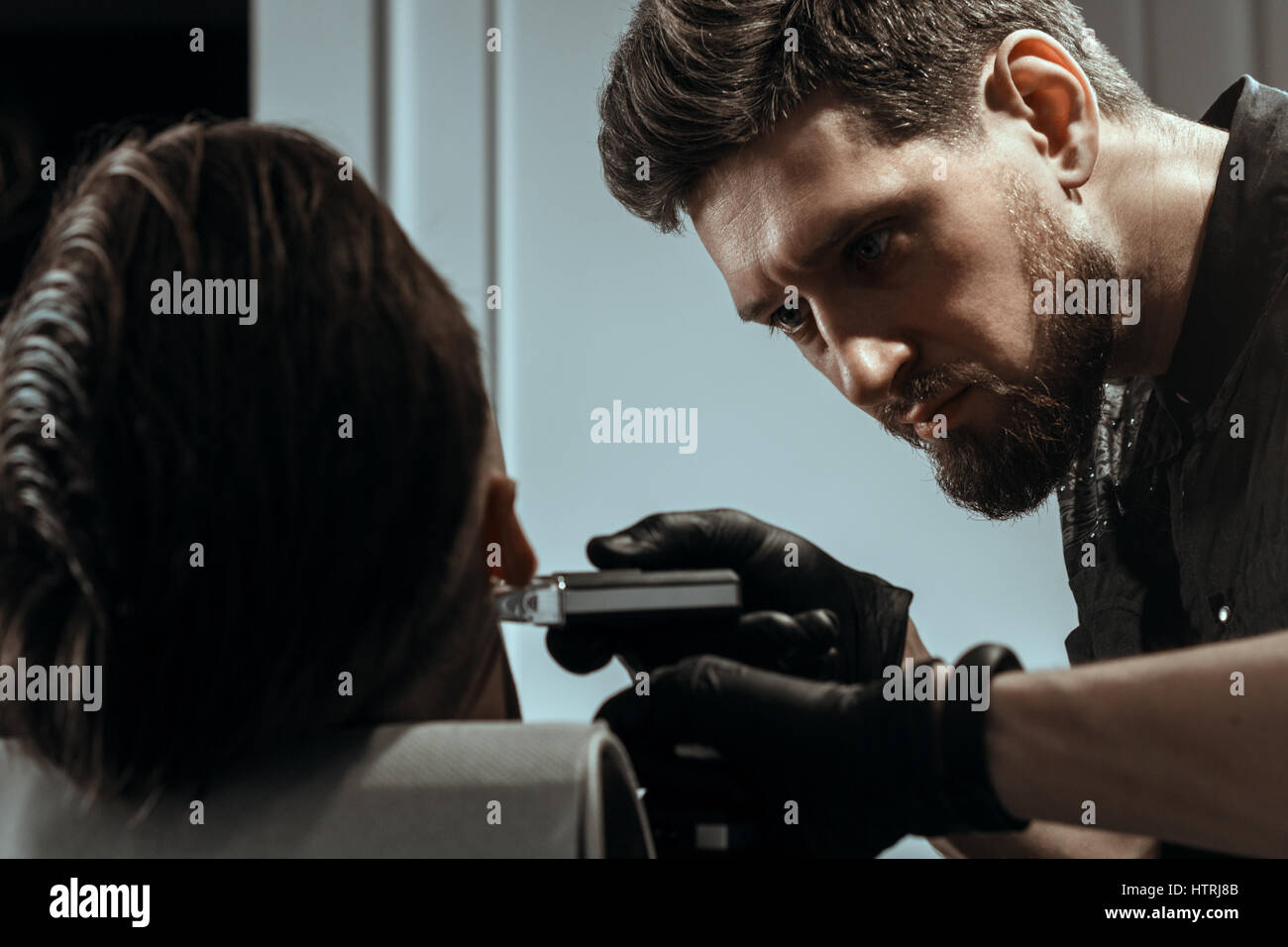 BARBERSHOP THEME. BEARDED BARBER IN BLACK RUBBER GLOVES IS TRIMMING THE