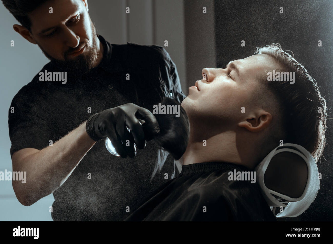BARBERSHOP THEME. BEARDED BARBER IN BLACK RUBBER GLOVES APPLIES TALC BY