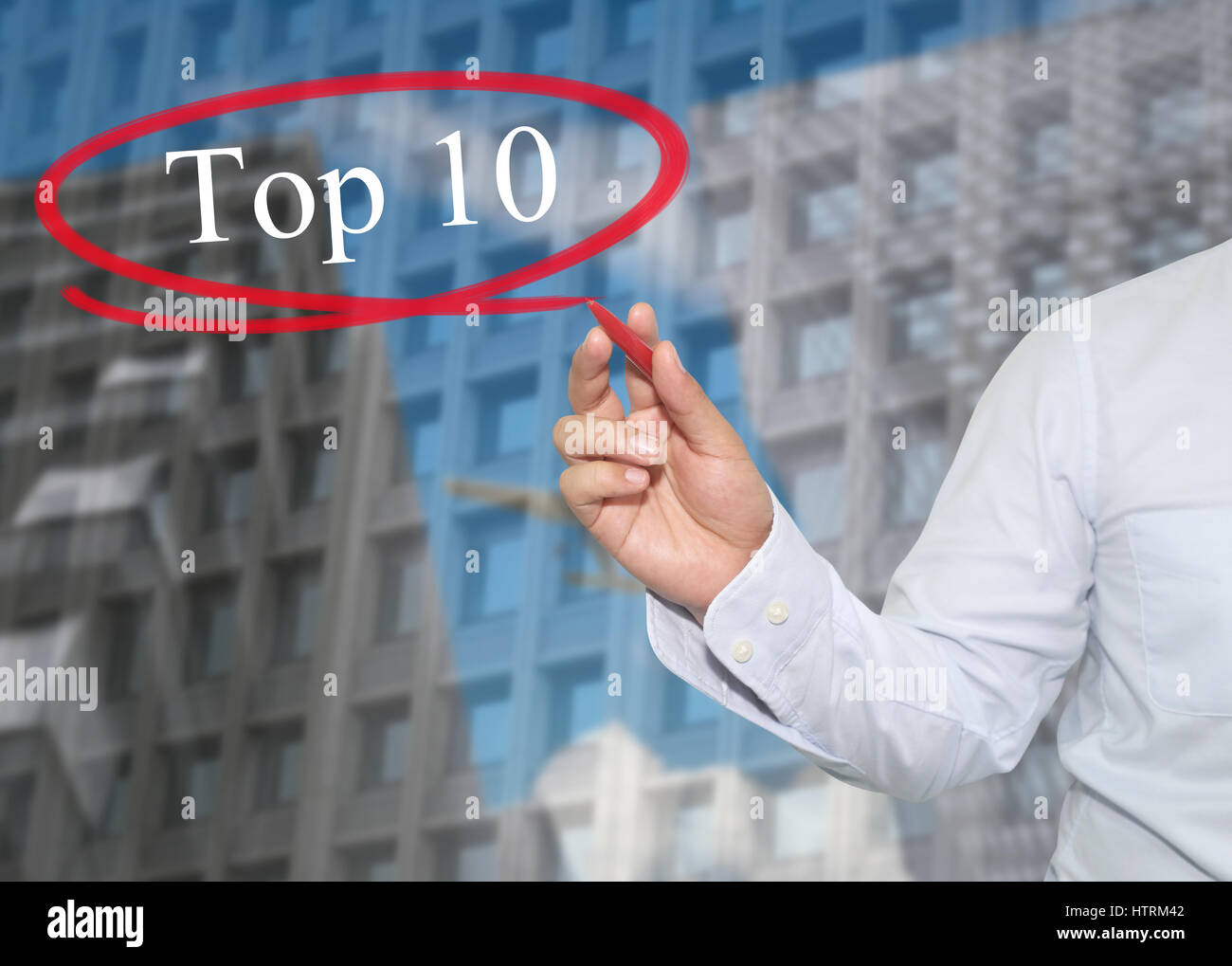 Hand of young businessman write the word Top 10 on skyscrapers background,concept of Apply to promote your business or work presentations. Stock Photo