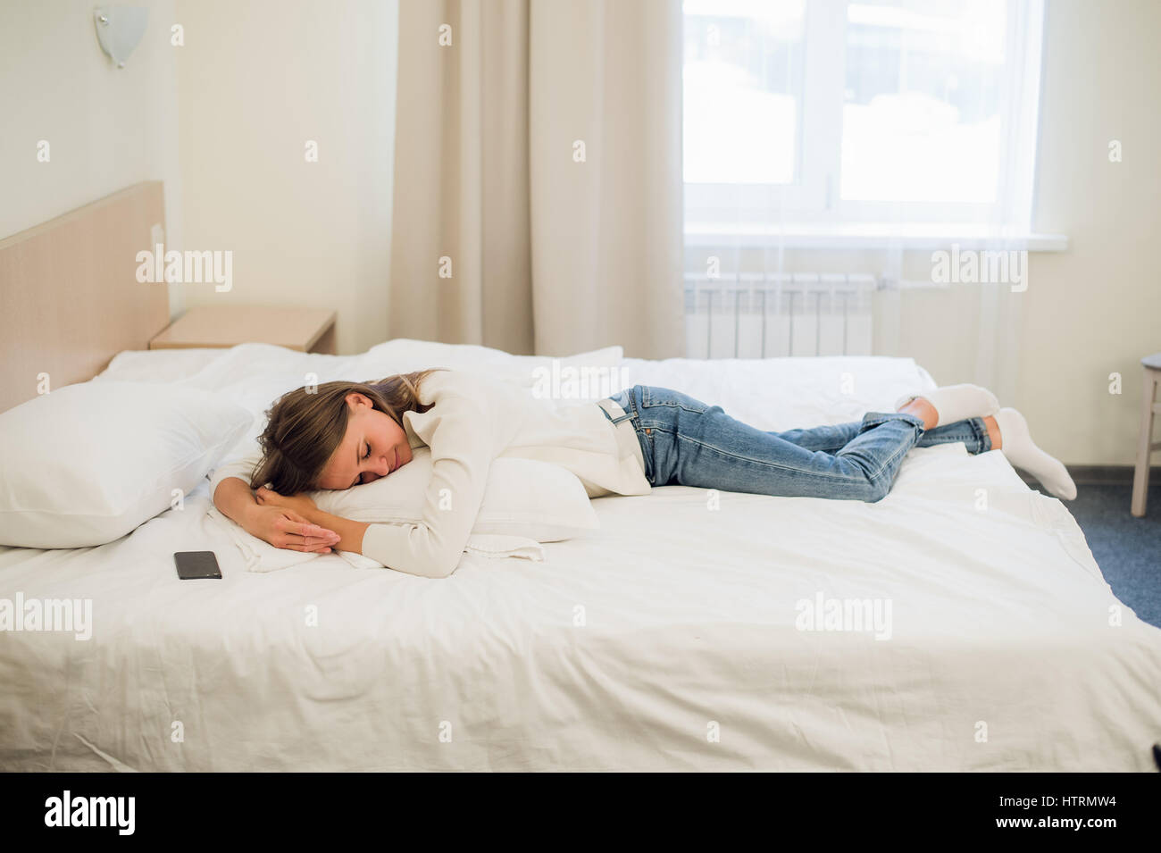 A woman laying on her bed still dressed in her clothes to tired to get in the bed. Stock Photo