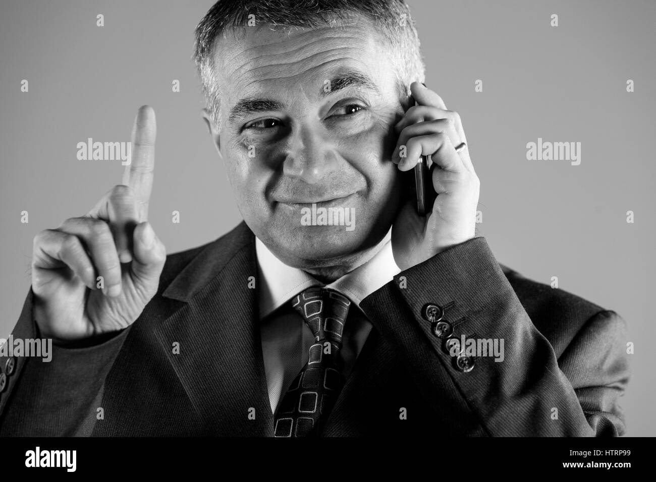 Businessman gesturing with his finger as he listens to a conversation on his mobile phone, close up cropped greyscale image Stock Photo