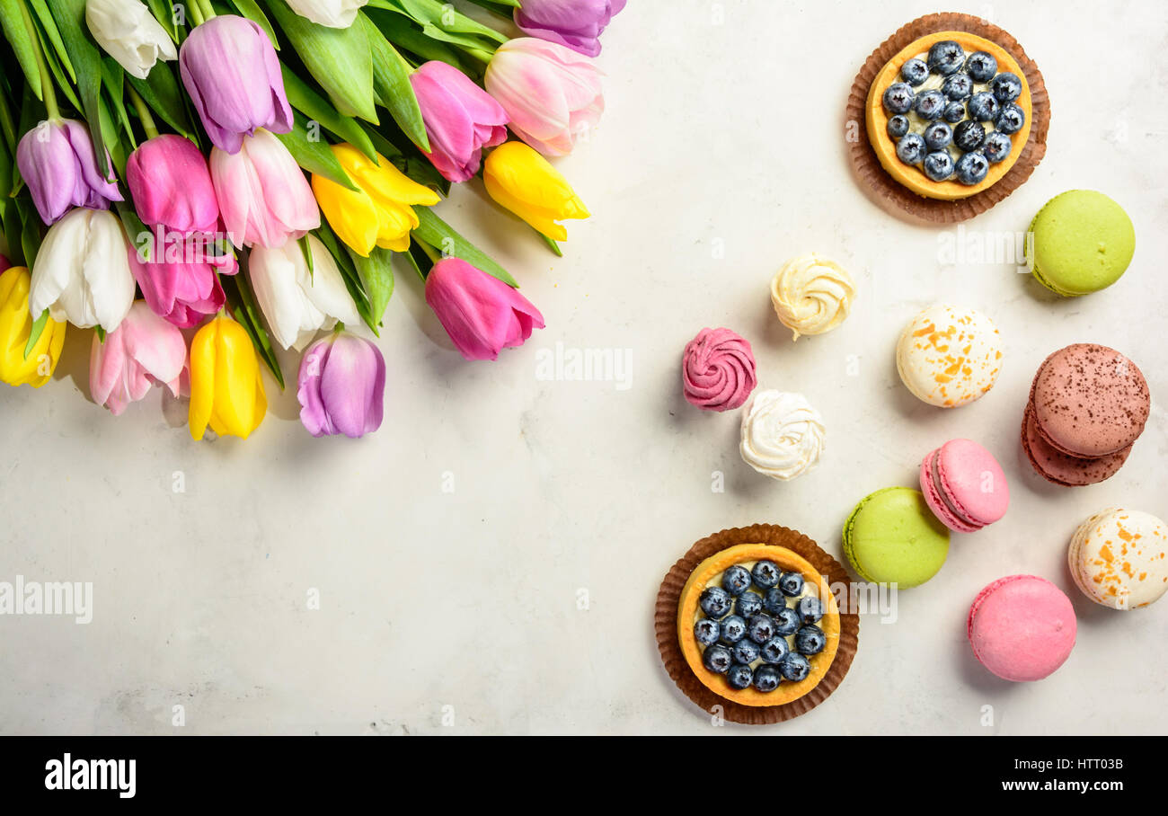 Beautiful festive bouquet of tulips and cakes on white background. Flat lay. Copy space. Stock Photo