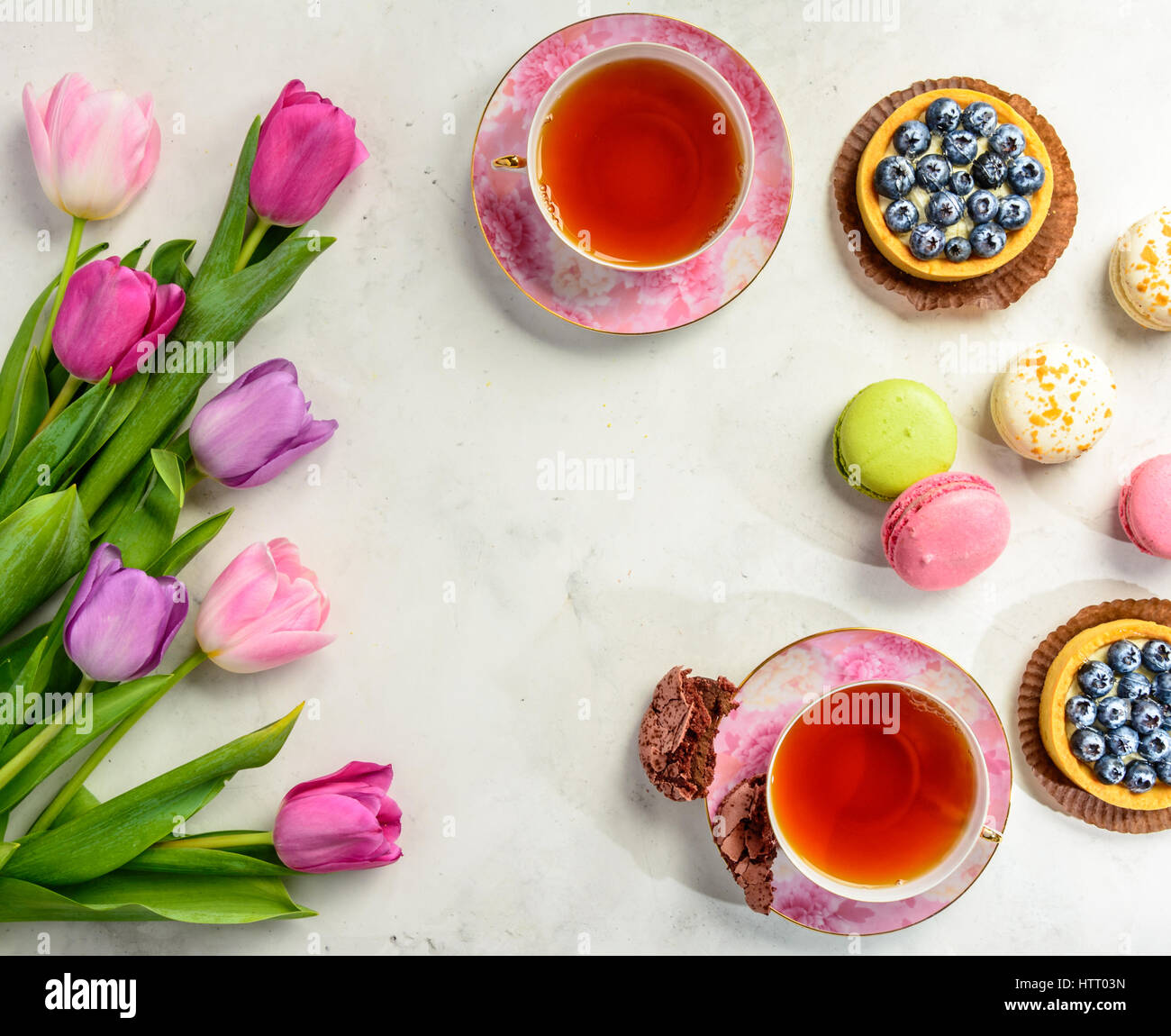 Beautiful festive bouquet of tulips, cakes and cup of tea on white background. Flat lay. Copy space. Stock Photo