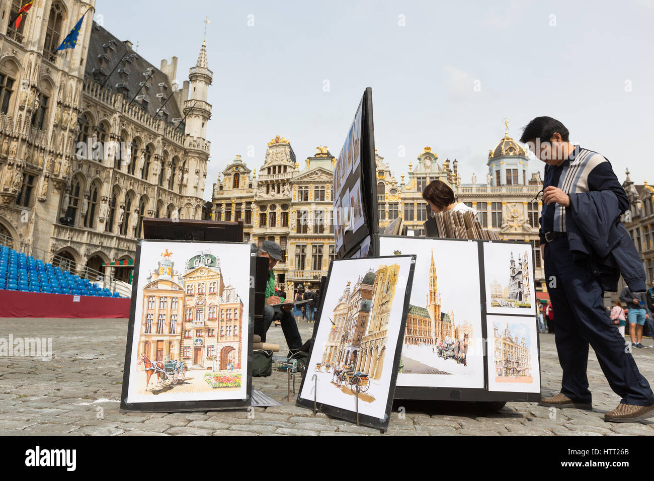 BRUSSELS, BELGIUM - JULY 6, 2016 - Tourists looking at paintings for sale in the Grand Place with the artist sitting sketching amongst his artwork. Stock Photo