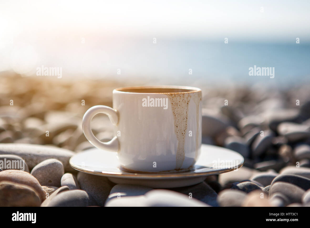 A cup of spilled coffee stands on stones near the sea shore, close up ...