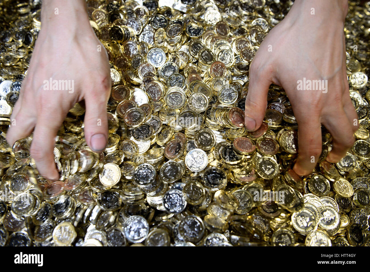 Editorial Use only &ETH; NO COMMERCIAL USE A worker grabs a handful of new 12-sided one pound coins from a metal crate as they are minted at the Royal Mint in Llantrisant, Wales. Stock Photo