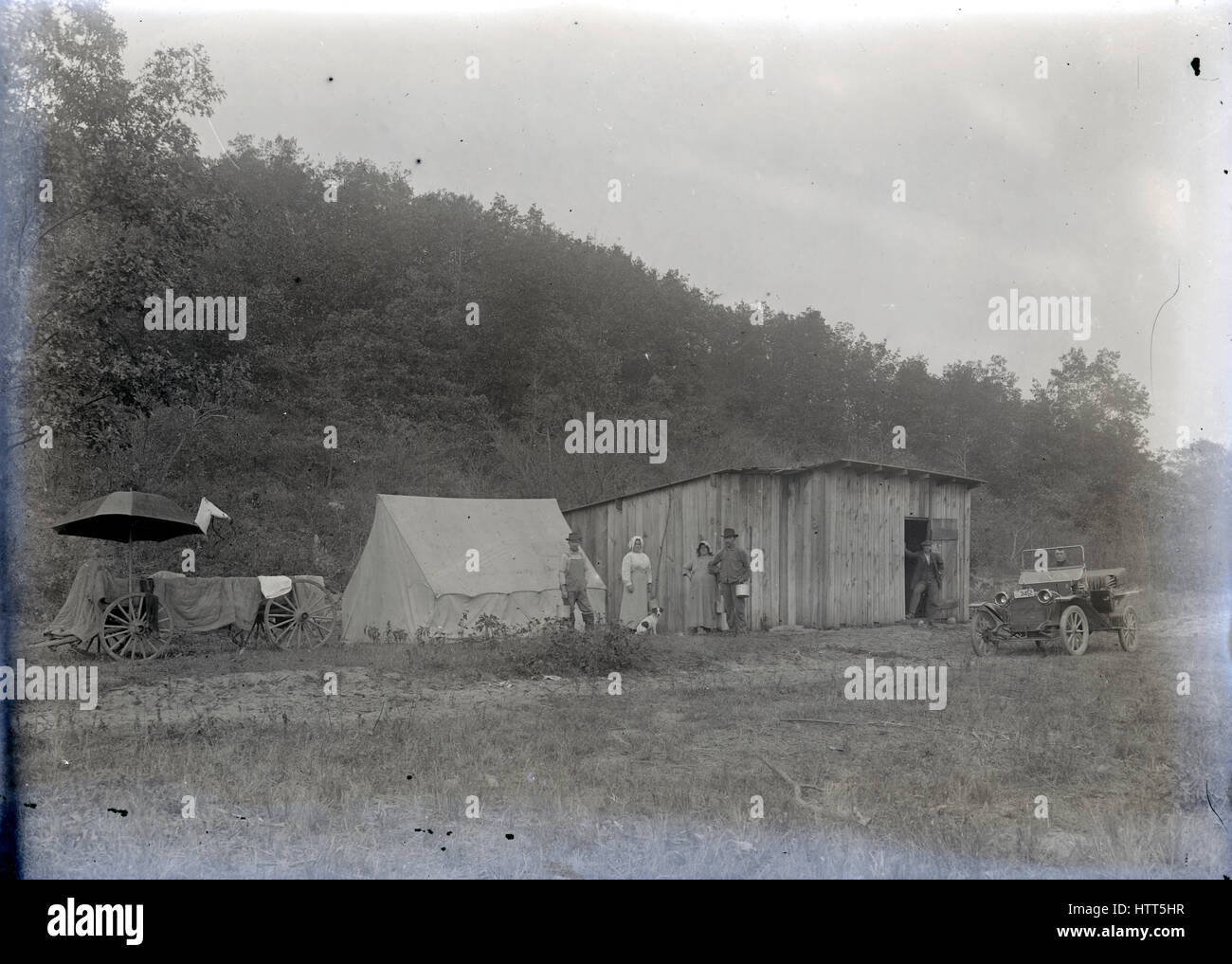 Antique c1914 photograph, men and women in a roadside wagon, tent, and wooden structure. The vehicle is a Studebaker with 1914 Michigan license plates. Location is Michigan, USA. SOURCE: ORIGINAL GLASS NEGATIVE. Stock Photo