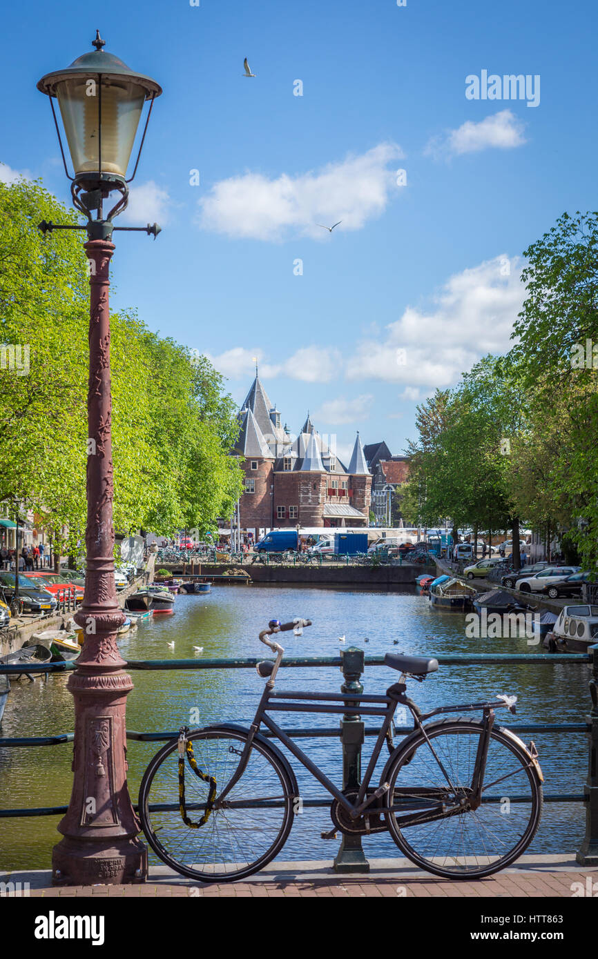Bike and lamp post on bridge over canal with city behind, typical scene in Amsterdam, The Netherlands Stock Photo